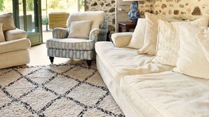 A living room with a stone wall, a sofa, a chair, and a patterned rug. - Les Picardies (Lesterps)