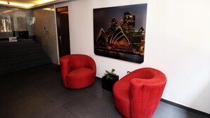 A lobby with two red chairs, a staircase, and a cityscape painting on the wall. - Oslo 10 (Mexico City)