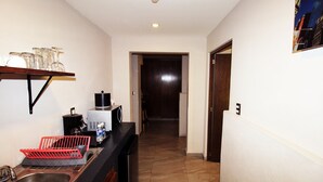 A narrow hallway with a kitchen area on the left, including a sink, a coffee maker, and a dish rack. - Oslo 10 (Mexico City)