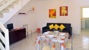 A modern living room with a dining area, white staircase, and two paintings on the wall. - Confort (Comacchio)