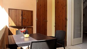 A patio with a table and chairs, wooden doors, and a glass door leading to an interior space. - Confort (Comacchio)