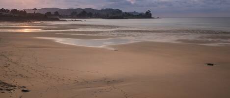 A beach with footprints leading to the water, a calm sea, and a sunset in the background.