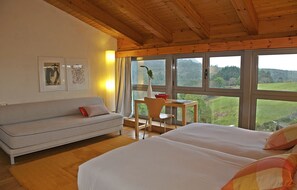 A room with a wooden ceiling, a sofa, a desk with a chair, and a bed. - Hotel El Babú (Caravia)
