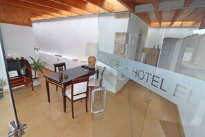 A modern hotel room with a wooden ceiling, a glass partition with "HOTEL EL BABU" signage, a dining area with a table and chairs, and a potted plant. - Hotel El Babú (Caravia)