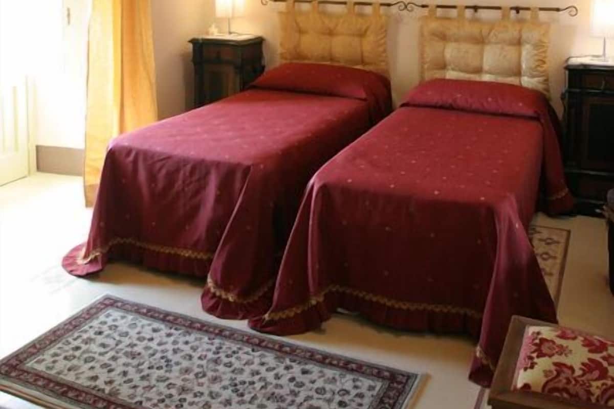 A room with two beds, a wooden ceiling, a painting on the wall, a lamp, and a patterned rug.