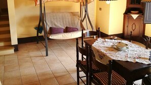 Un coin repas avec une table en bois dressée pour quatre personnes, un banc recouvert d’un tissu à carreaux et un plafond rustique.