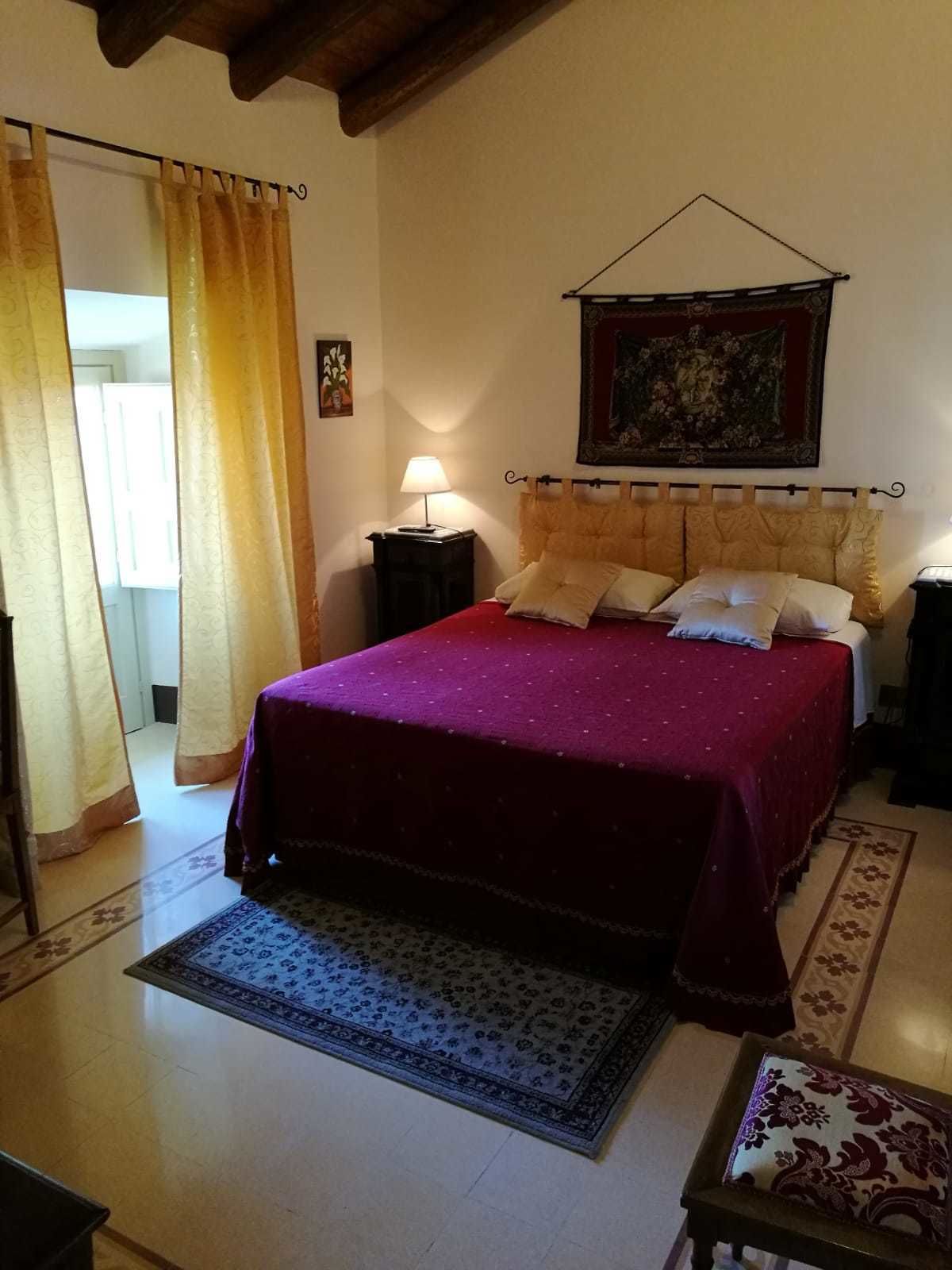 A bedroom with a bed, a nightstand, a lamp, a painting, and a patterned rug.