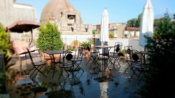 Une terrasse extérieure avec des tables et des chaises, une fontaine et, au fond, un bâtiment en forme de dôme.