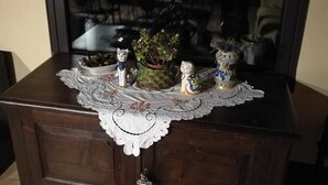 Un meuble en bois orné d’une nappe en dentelle, d’une plante en pot et de quelques objets décoratifs.