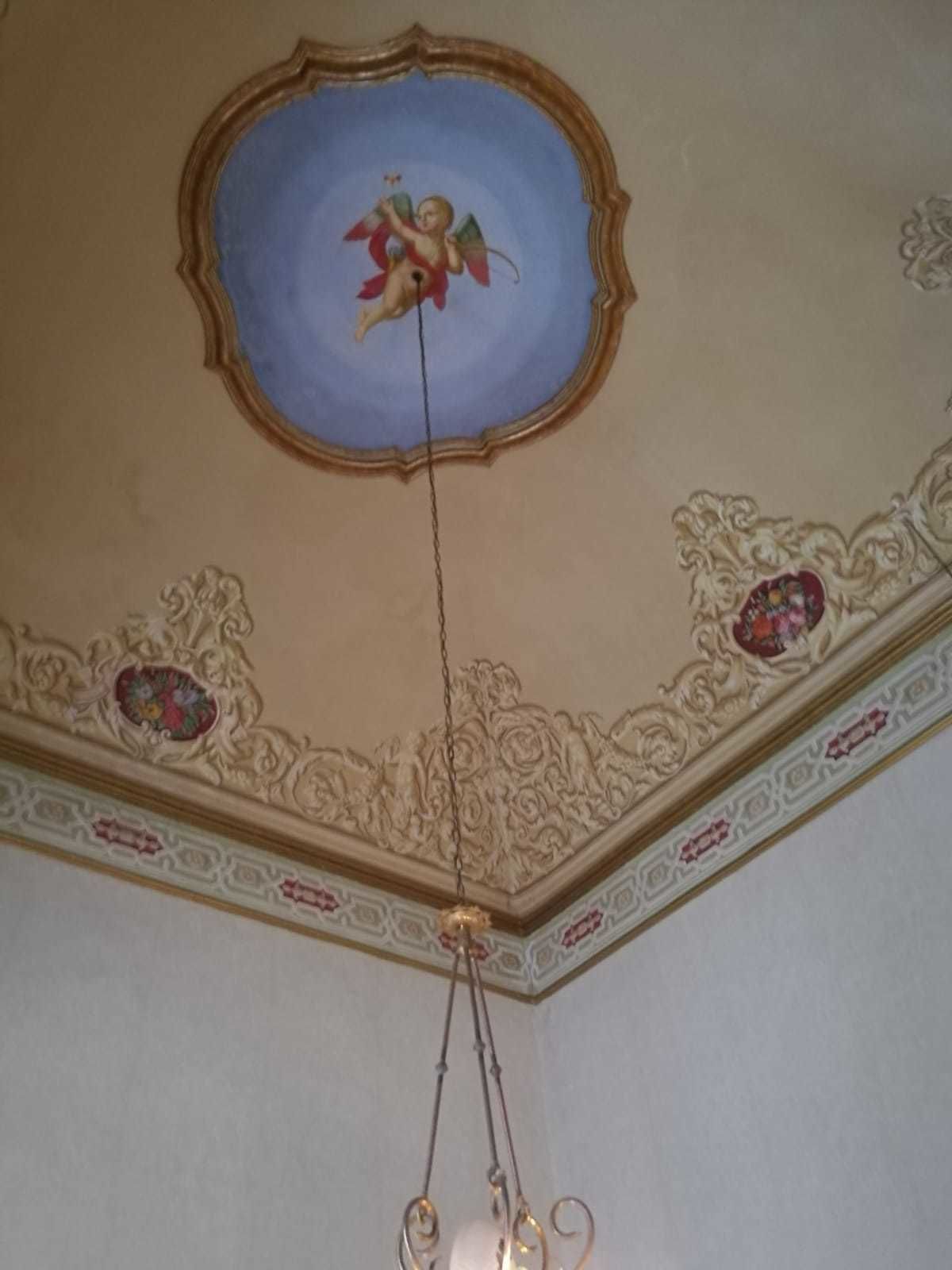 Ett tak med en målad putto, utsmyckade lister och en hängande lampa.