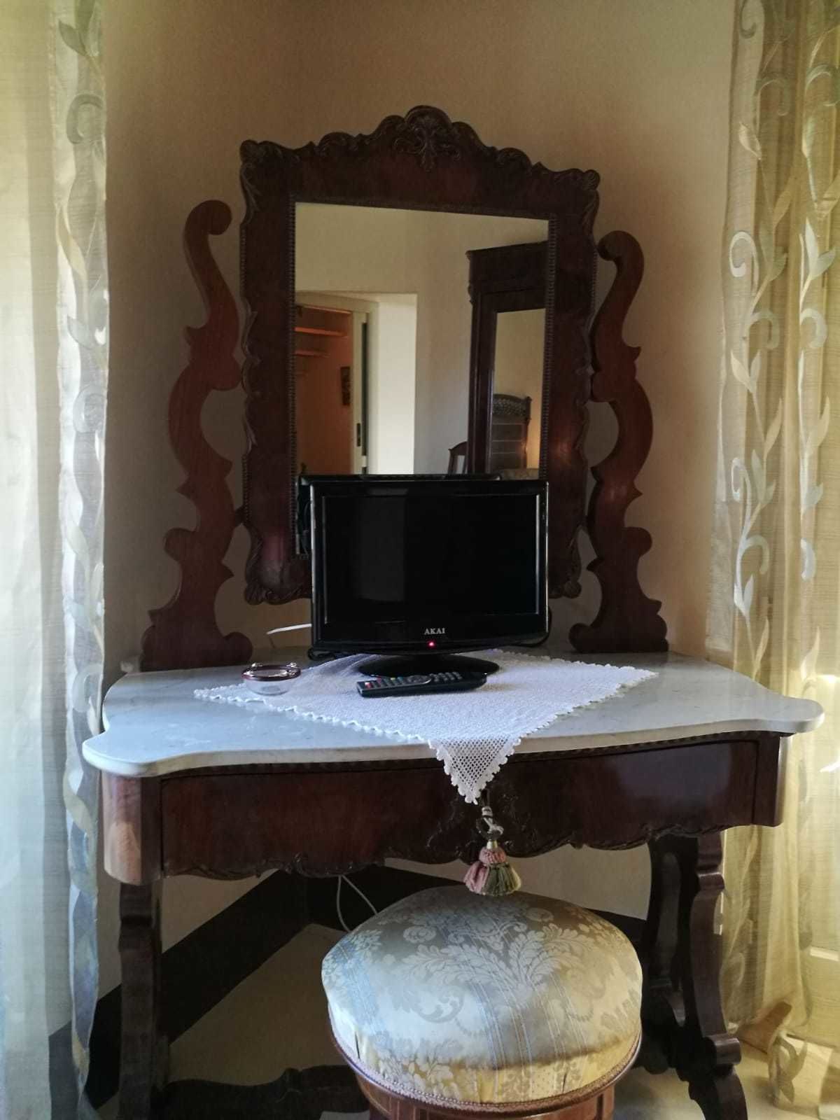 Un tocador de madera con espejo, un televisor y un taburete decorativo.