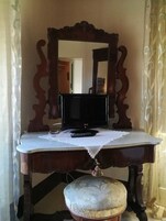 Un tocador de madera con espejo, un televisor y un taburete decorativo.