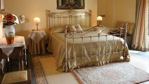 Une chambre à coucher avec un lit, deux tables de chevet, une commode, une grande moquette, un tableau encadré au mur et une fenêtre avec des rideaux.