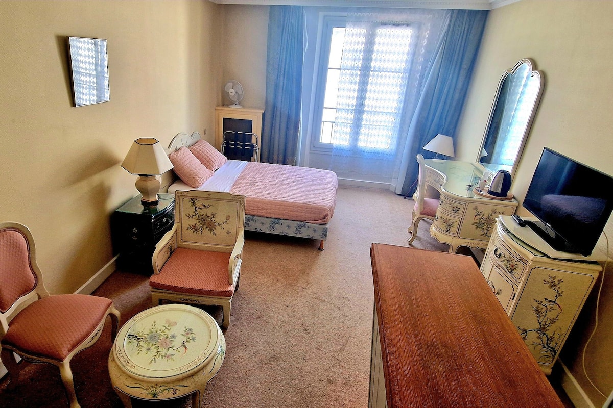 Une chambre d’hôtel avec un lit, une chaise, une petite table, un téléviseur et une commode.