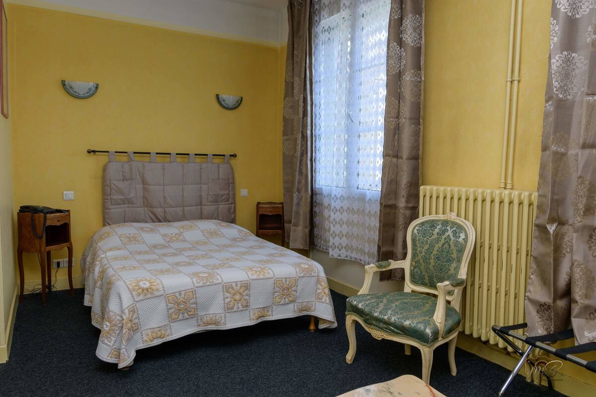 Une chambre à coucher avec un lit, une chaise, un radiateur et une fenêtre avec des rideaux.