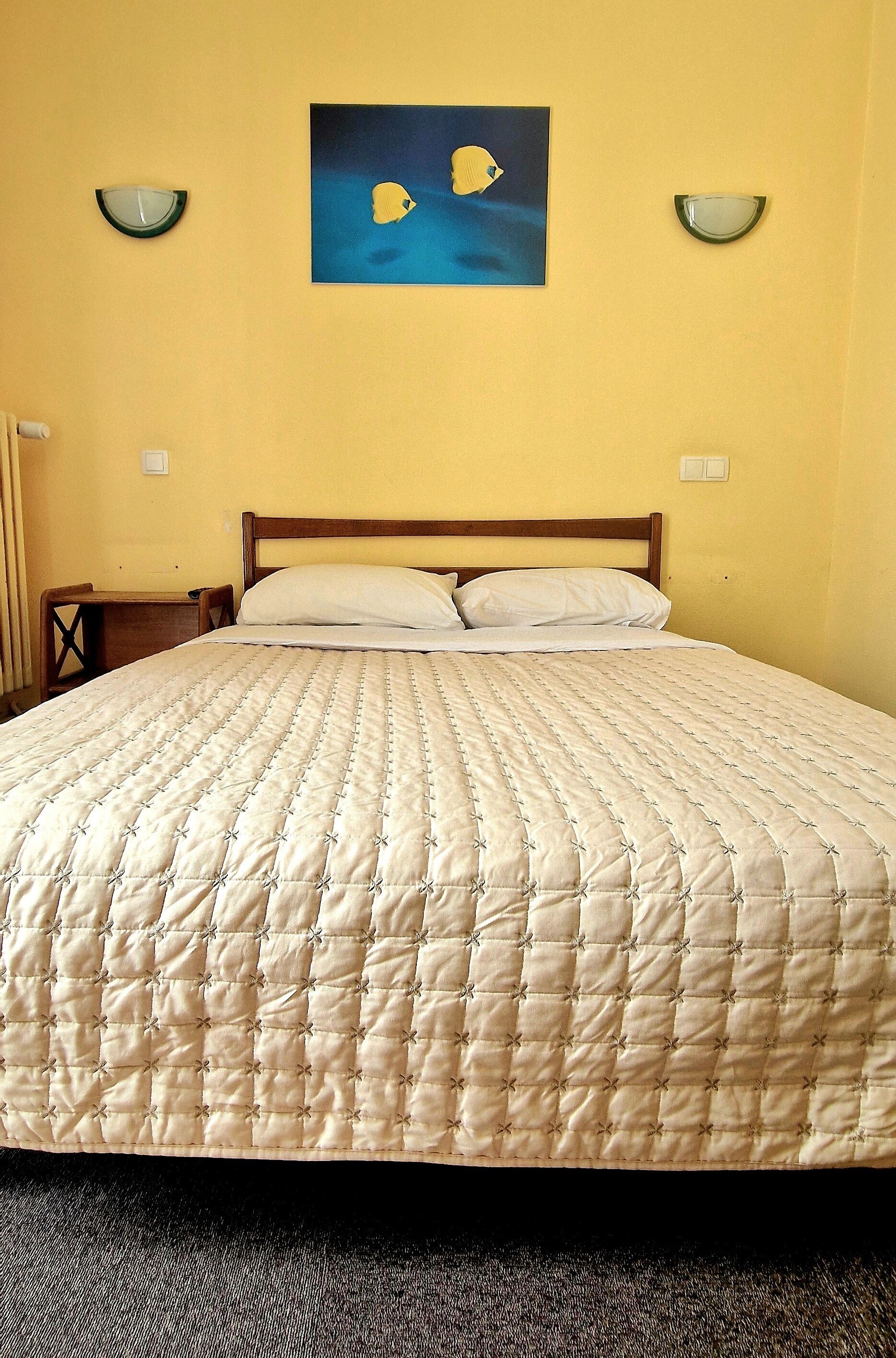 A bed with a quilted beige cover, a wooden headboard, and two wall-mounted light fixtures.