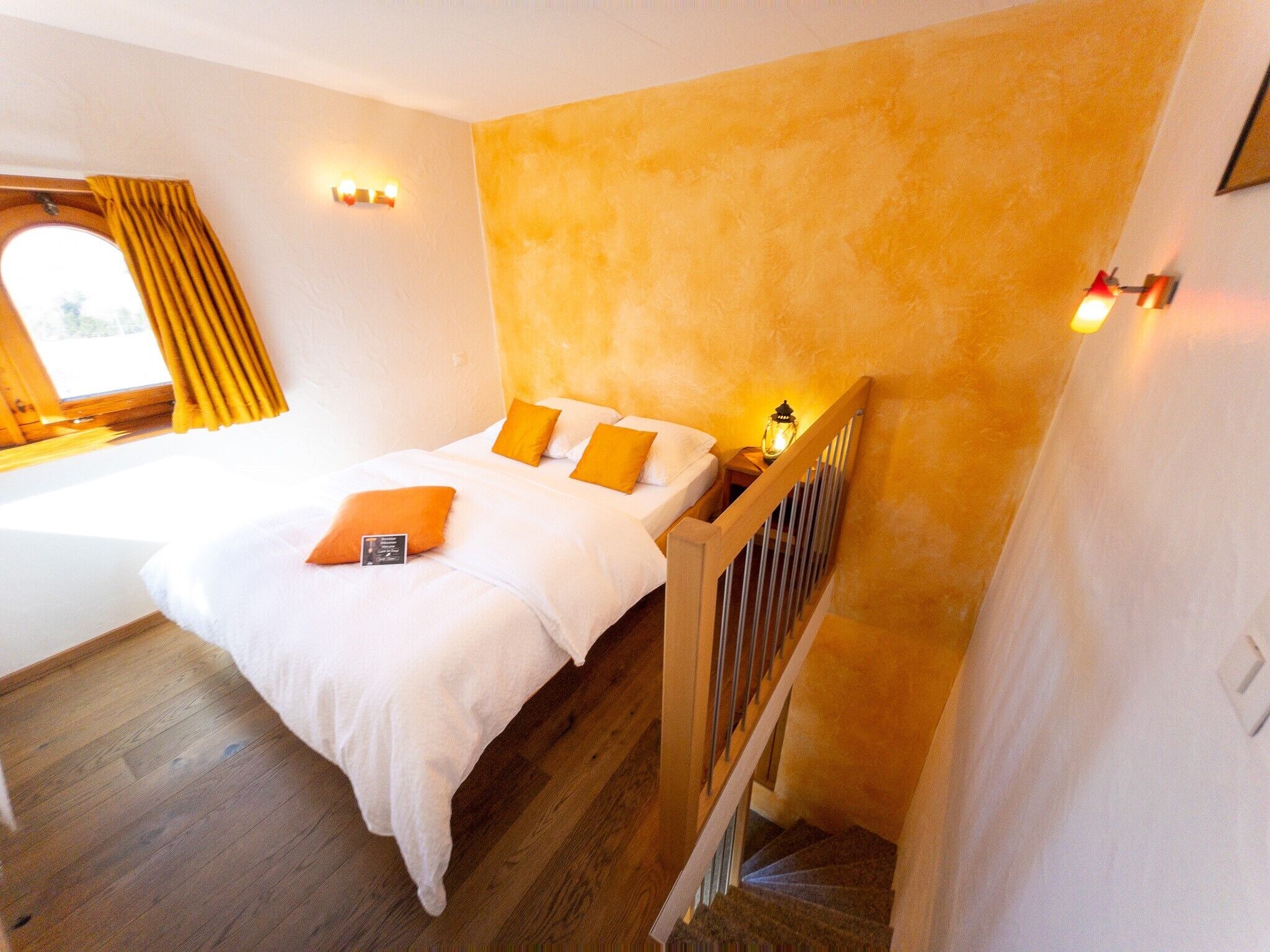 A bedroom with a bed, wooden floor, and a staircase.