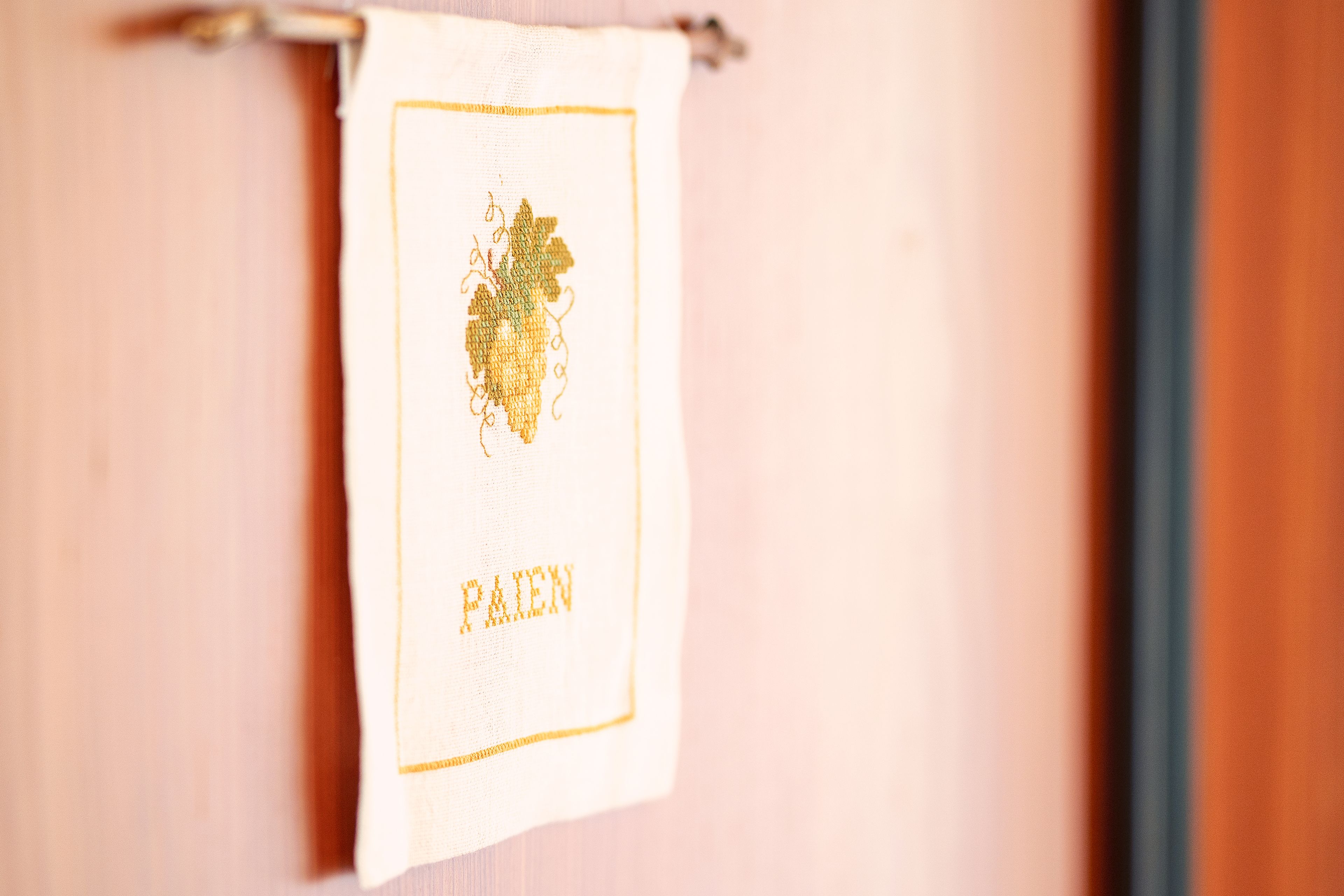 A white towel with a gold embroidered design and the word "PAID" hanging on a wooden surface.