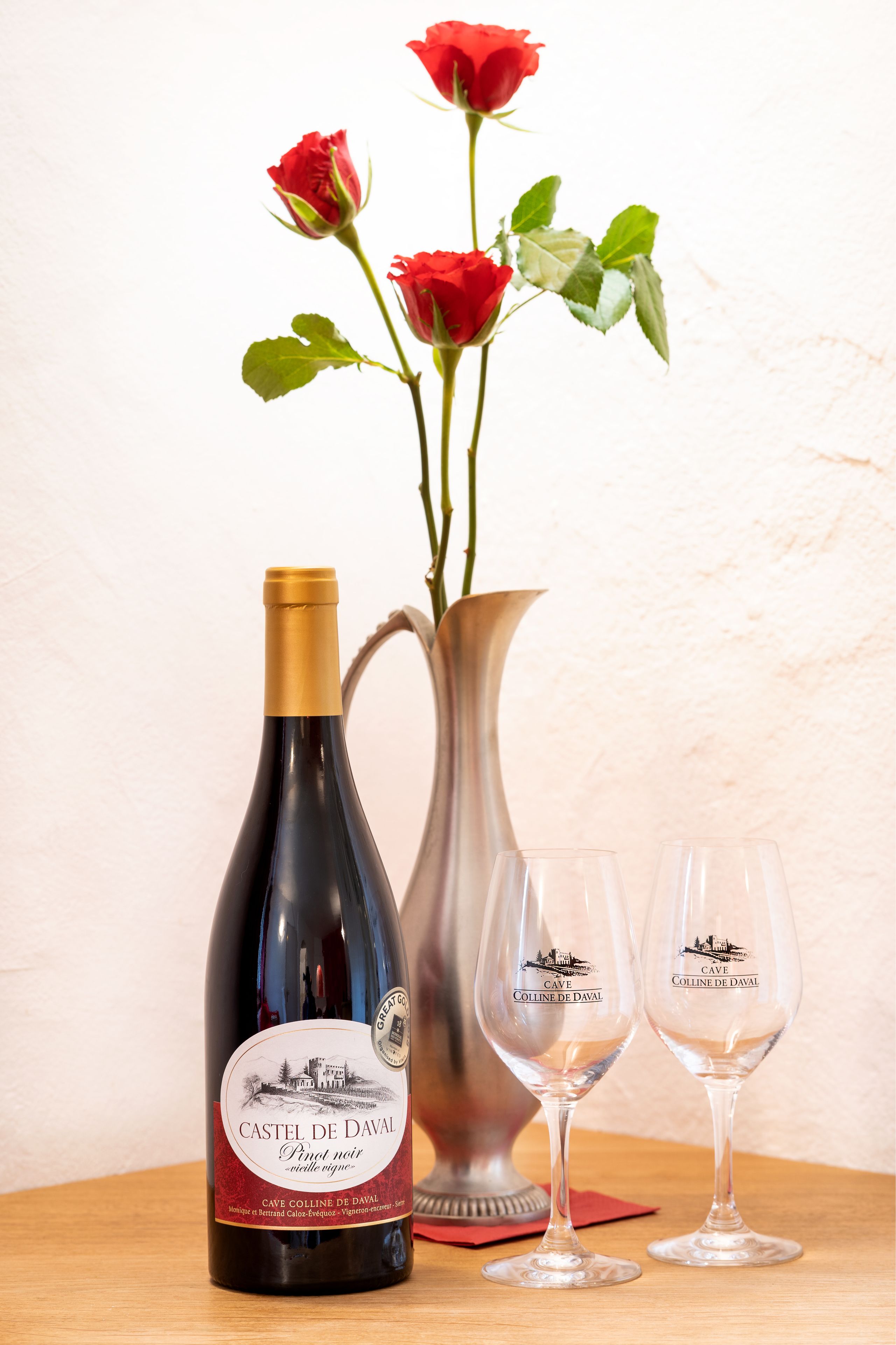 A bottle of wine, two wine glasses, and a vase with roses.