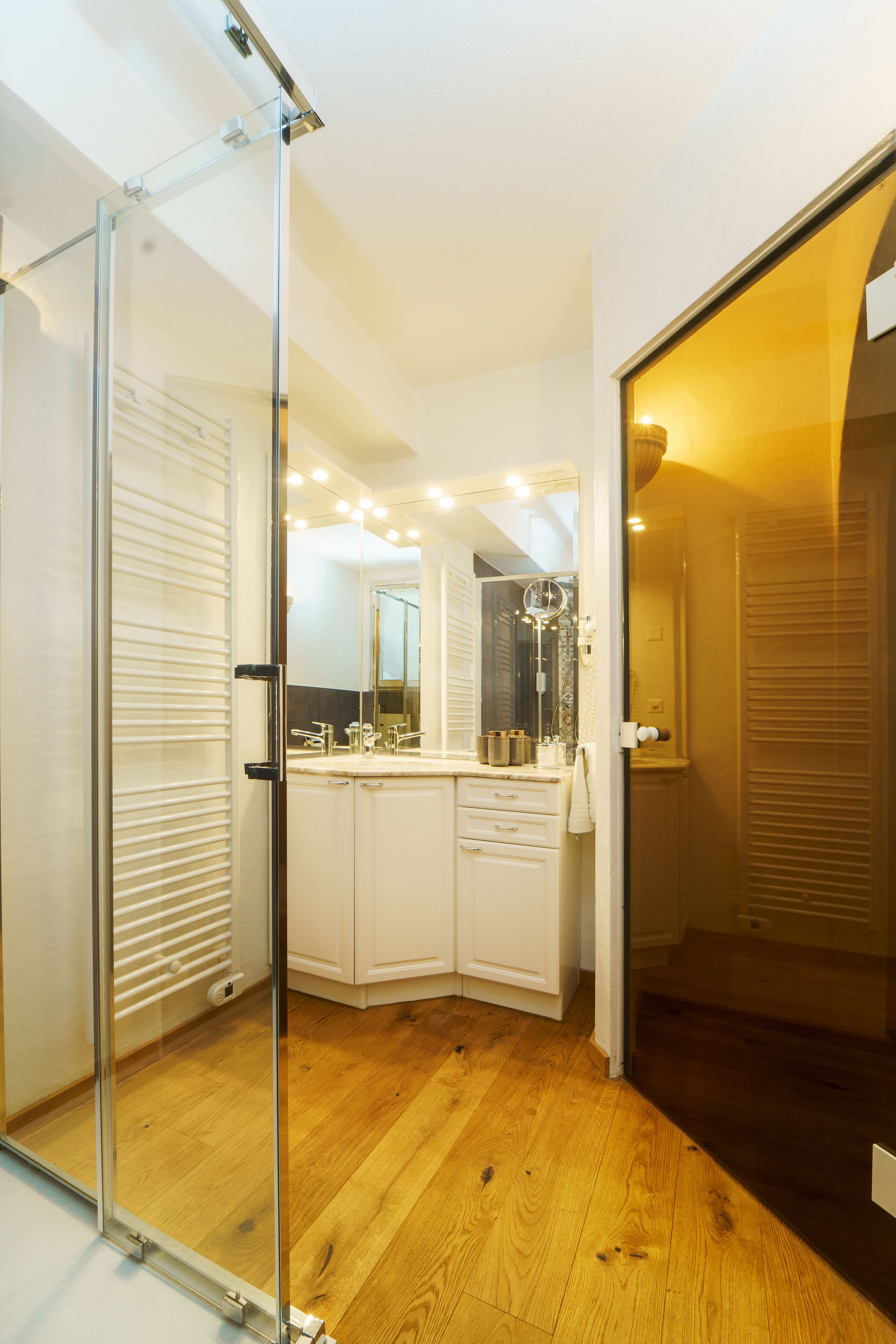 A modern bathroom with a glass shower enclosure, white cabinetry, and a large mirror.