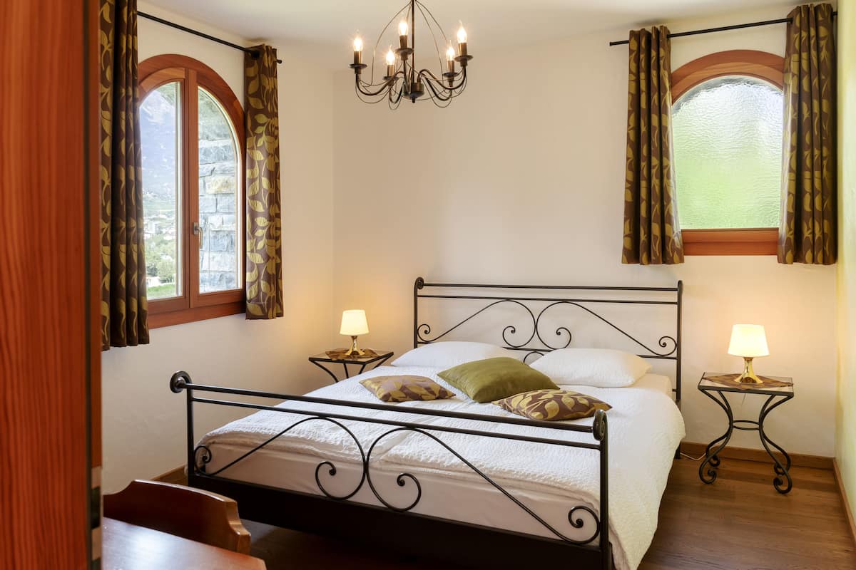 A neatly arranged bedroom with a four-poster bed, two bedside tables with lamps, and a chandelier.