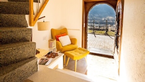A staircase with wooden railings leading to a living area with a yellow armchair and ottoman, a lamp, and a view through an arched doorway. - Castel de Daval (Sierre)