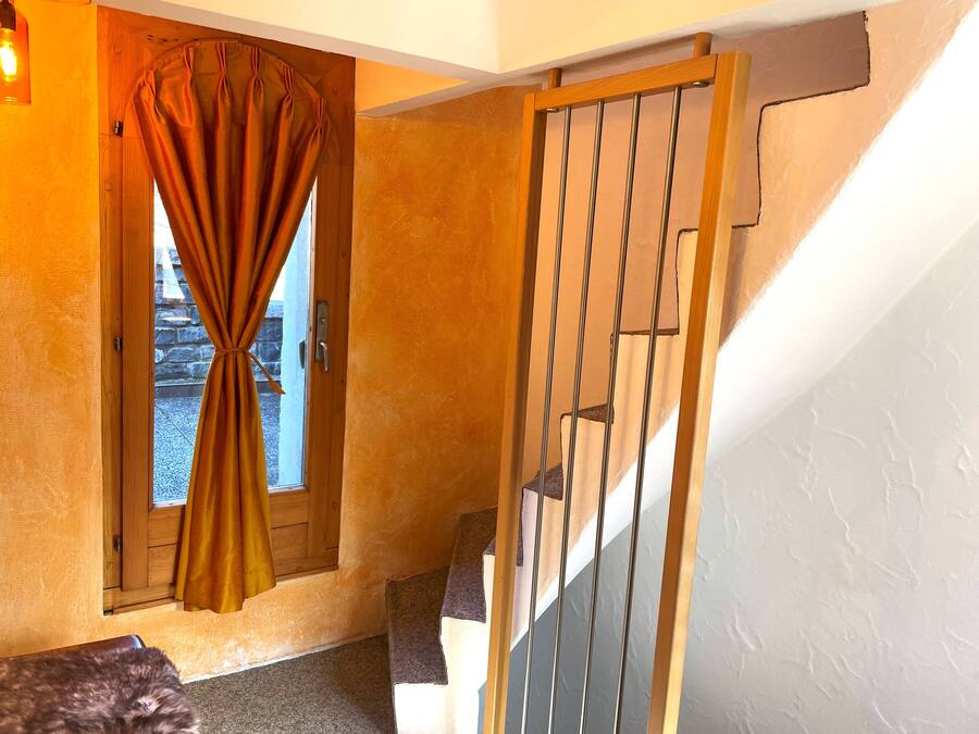 Una escalera de madera con barandilla de metal, una puerta con cortina y una pared de piedra visible a través de la puerta.