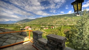 A scenic view from a balcony with a stone railing, a wooden floor, and a black metal lantern. - Castel de Daval (Sierre)