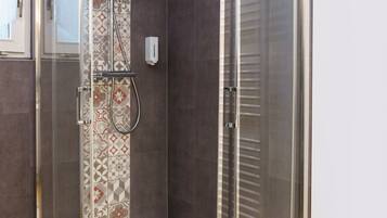 A glass-enclosed shower with a patterned tile wall, a wooden floor, and a white ceiling.