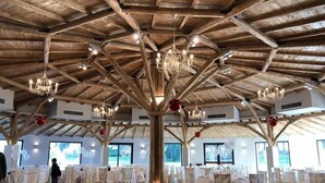 Une vaste salle dotée de hauts plafonds en bois et de lustres, aménagée pour un événement formel avec des tables et des chaises.