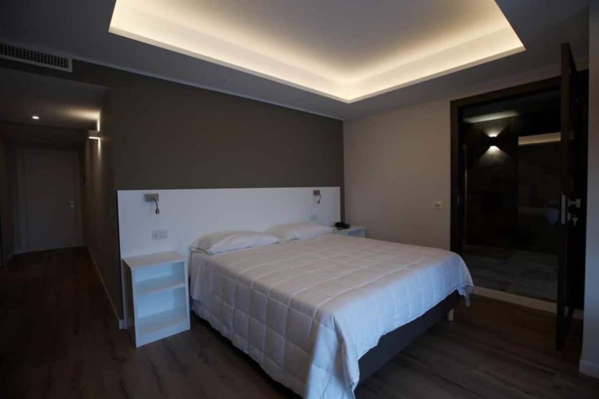 Un dormitorio moderno con cama, mesitas de noche y puerta de cristal que da a un balcón.