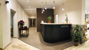 Un espace d’accueil d’hôtel avec un comptoir noir, des plantes en pot et un aménagement intérieur moderne.