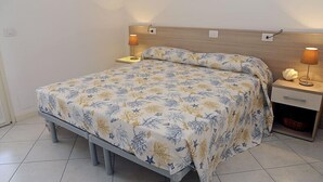 Ein Bett mit floralem Überwurf, ein Nachttisch mit Lampe und ein Beistelltisch ebenfalls mit Lampe.