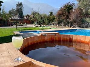 Een hottub met houten rand, een glas helder drankje en een zwembad op de achtergrond.