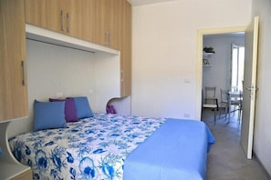 A bedroom with a bed, a wooden wardrobe, and a door leading to a dining area. - Tigli Piano Terra (Comacchio)
