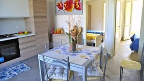 Et moderne køkken med spiseplads, med et bord med stole, en vase med tørrede planter, og et maleri af blomster på væggen.