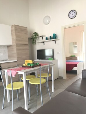A modern kitchen with a dining area, a TV, and a clock on the wall. - Tigli Piano Primo (Comacchio)