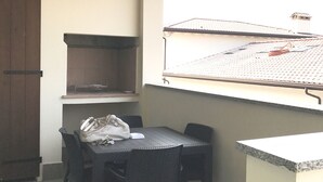 Un pequeño comedor con una mesa y sillas, una ventana con vista al tejado, y una puerta de madera.