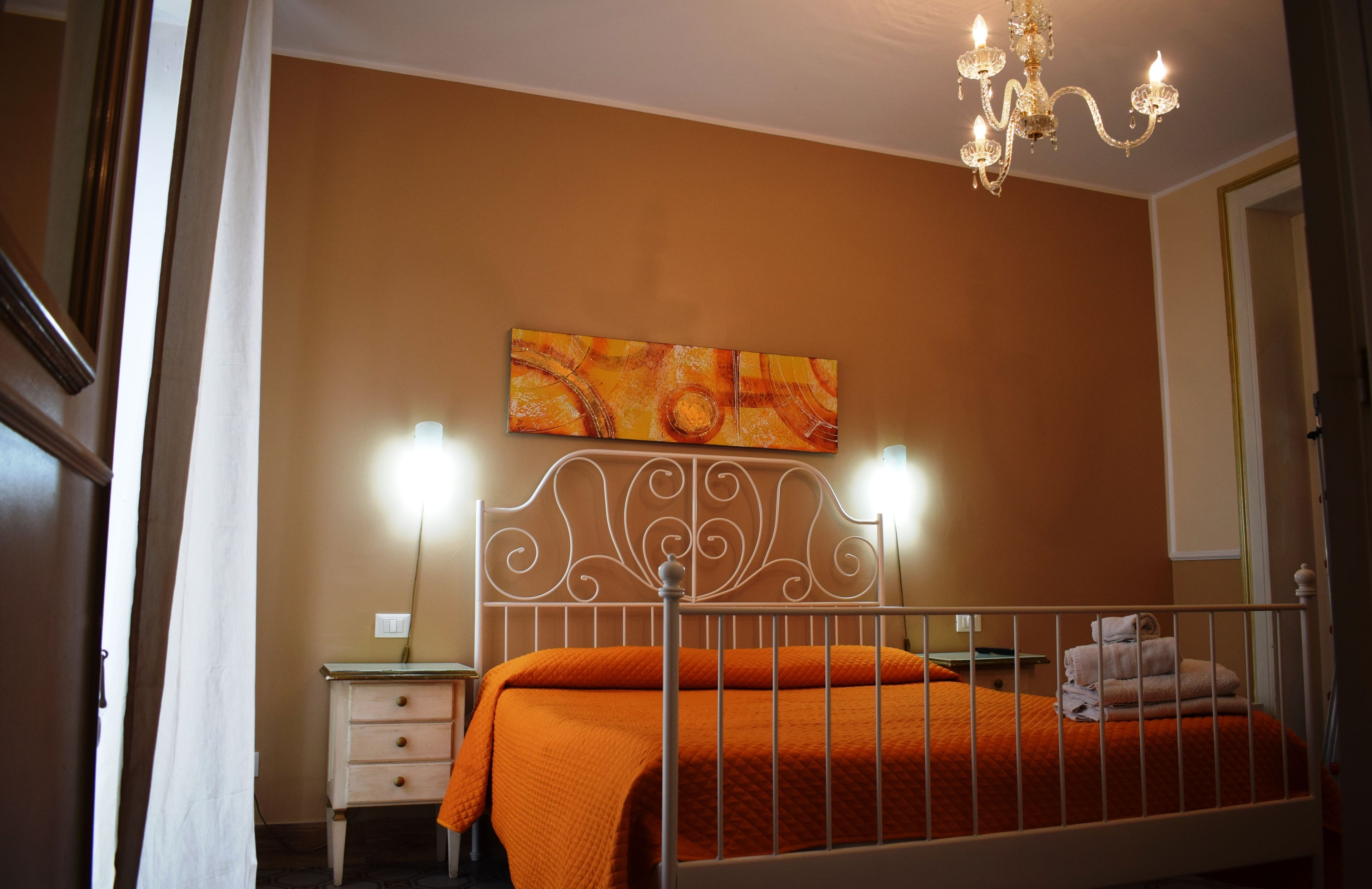 A bedroom with a bed, a nightstand, a wall-mounted painting, and a chandelier.