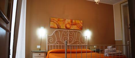 A bedroom with a bed, a nightstand, a wall-mounted painting, and a chandelier.