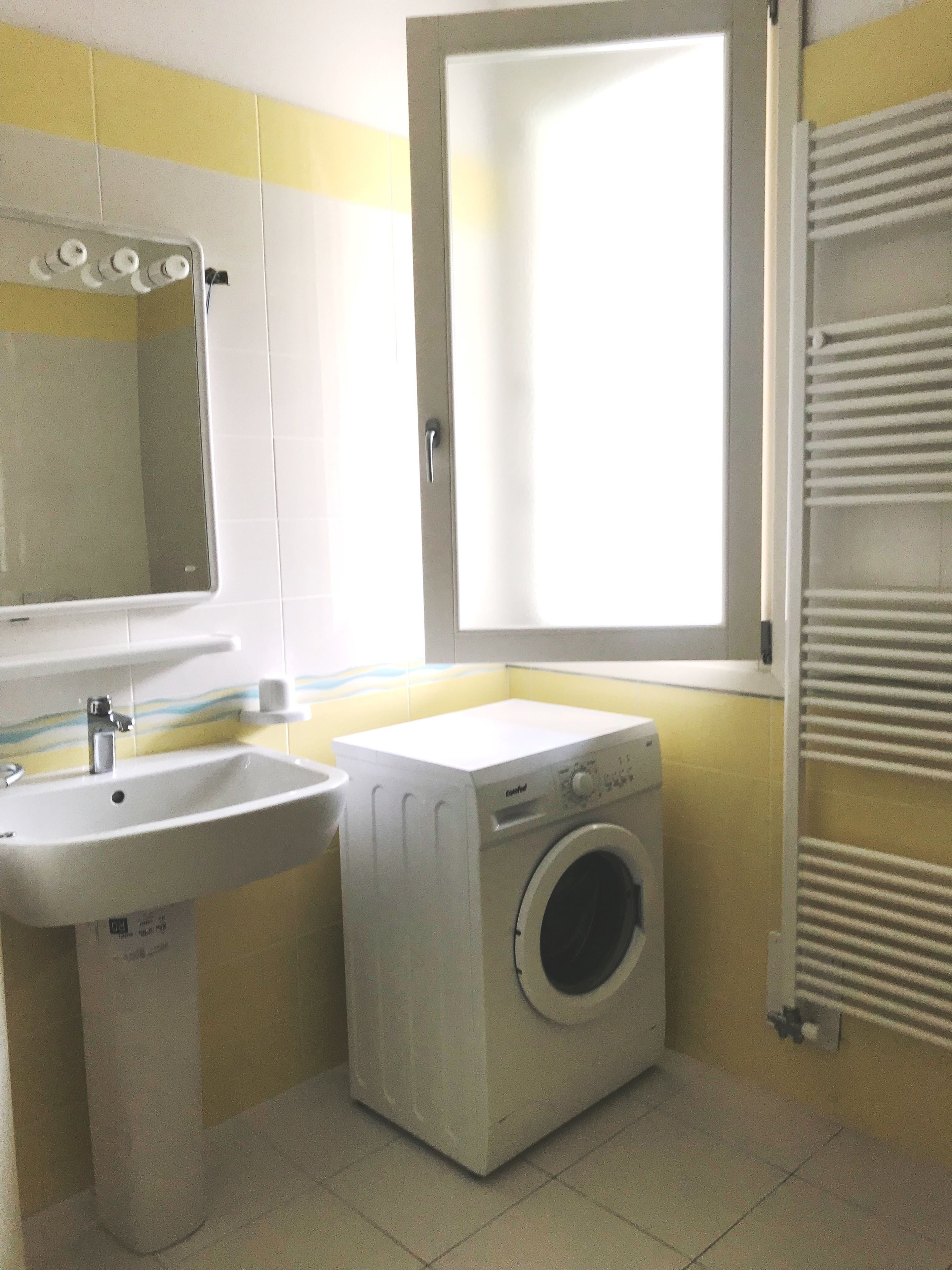 Un baño pequeño con lavamanos, lavadora y ventana.