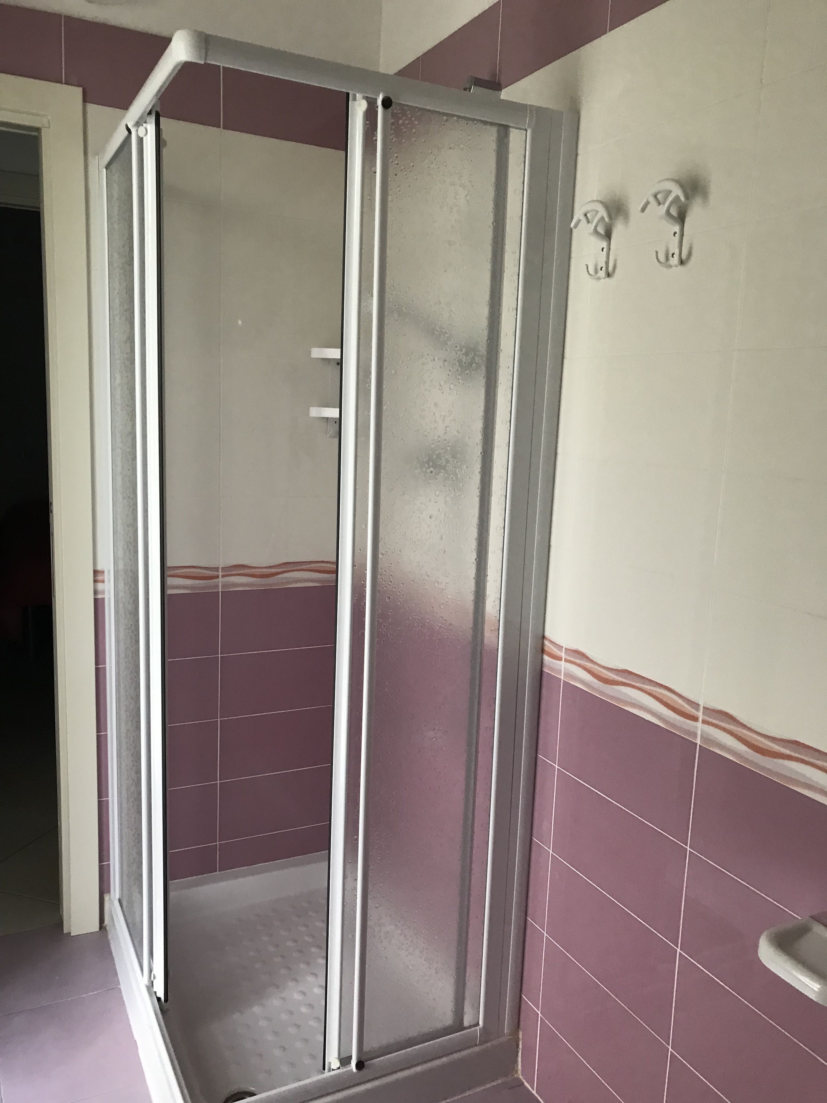 A shower enclosure with a glass door, a tiled wall with a horizontal stripe pattern, and a white towel rack on the wall.