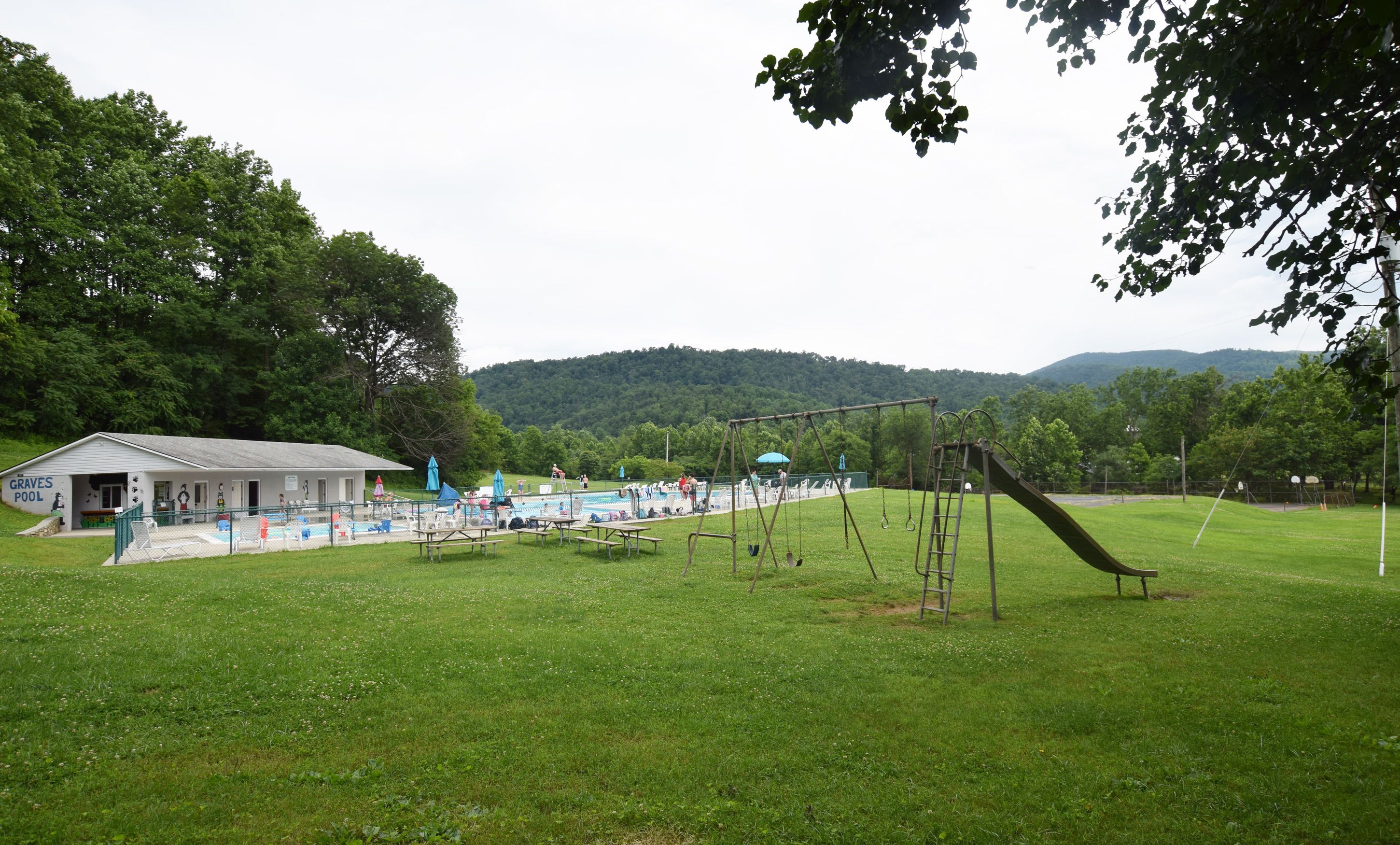 Un parque con piscina, mesas de picnic, un arenero y un parque infantil.