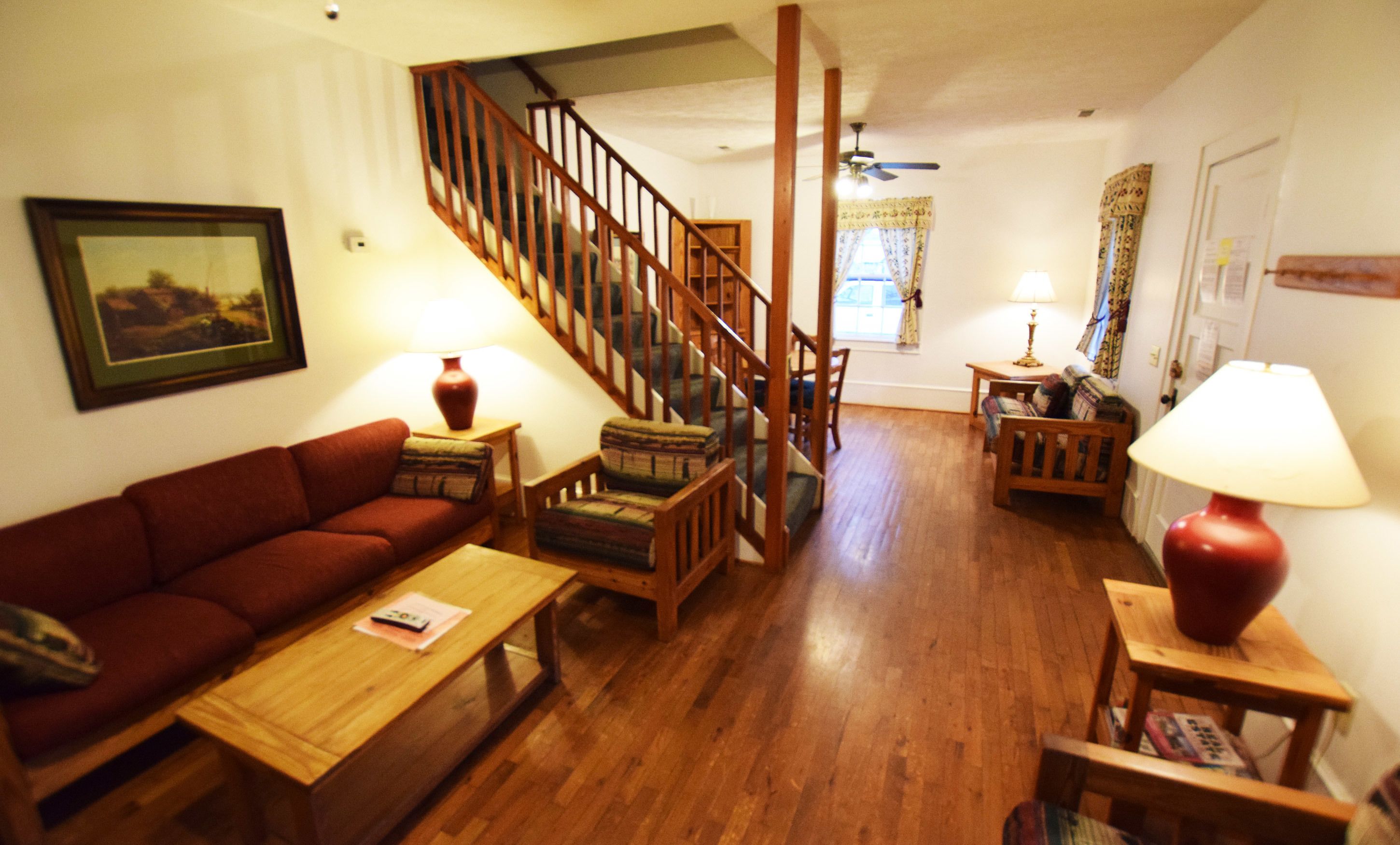 Ein Wohnzimmer mit einer Holztreppe, einem roten Sofa, einem Holztisch und zwei Lampen.