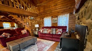 A log cabin interior with a red sofa, a wooden coffee table, a fireplace, and a staircase. - Graves Mountain Farm & Lodges (Syria)