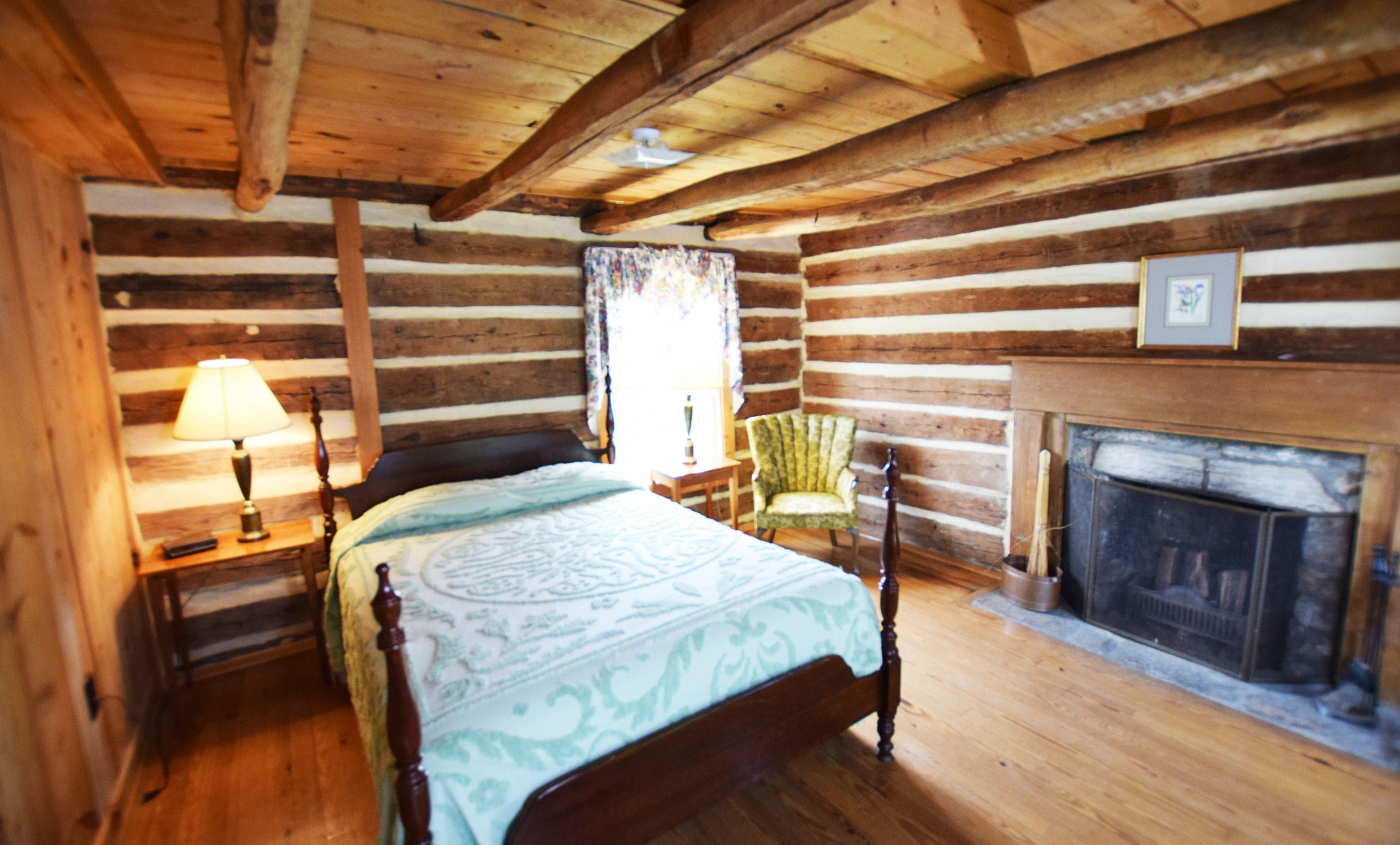 A log cabin bedroom with a bed, a chair, a lamp, and a fireplace.