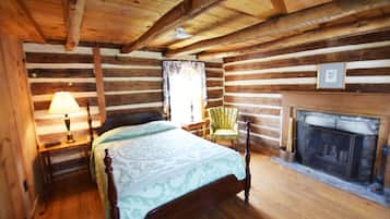 A log cabin bedroom with a bed, a chair, a lamp, and a fireplace.