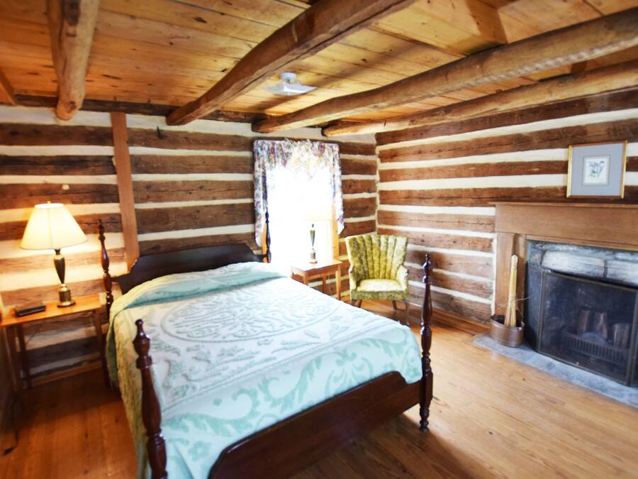 A log cabin bedroom with a bed, a chair, a lamp, and a fireplace.