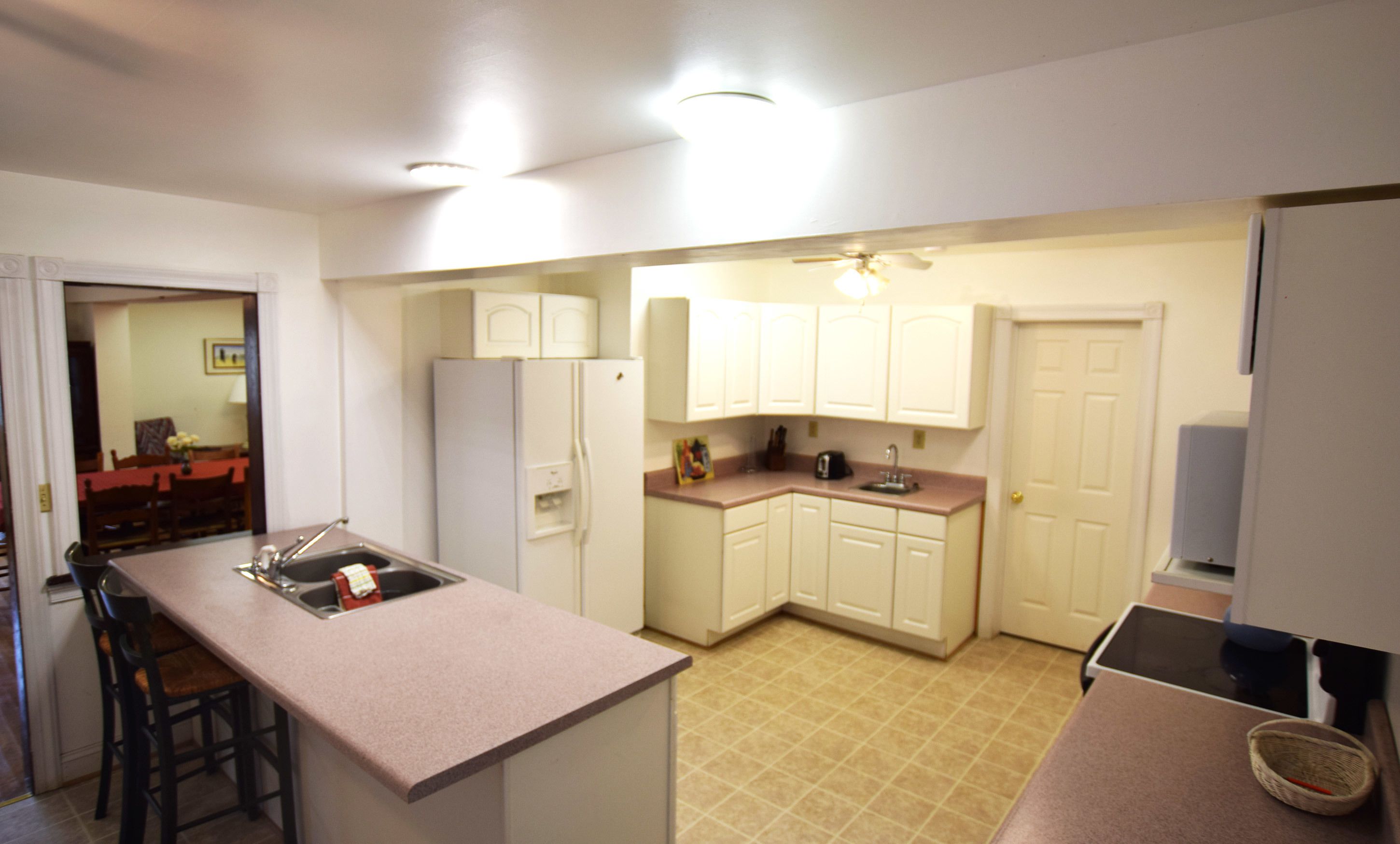 A compact kitchen with white cabinets, a refrigerator, a sink, and a dining area with chairs.
