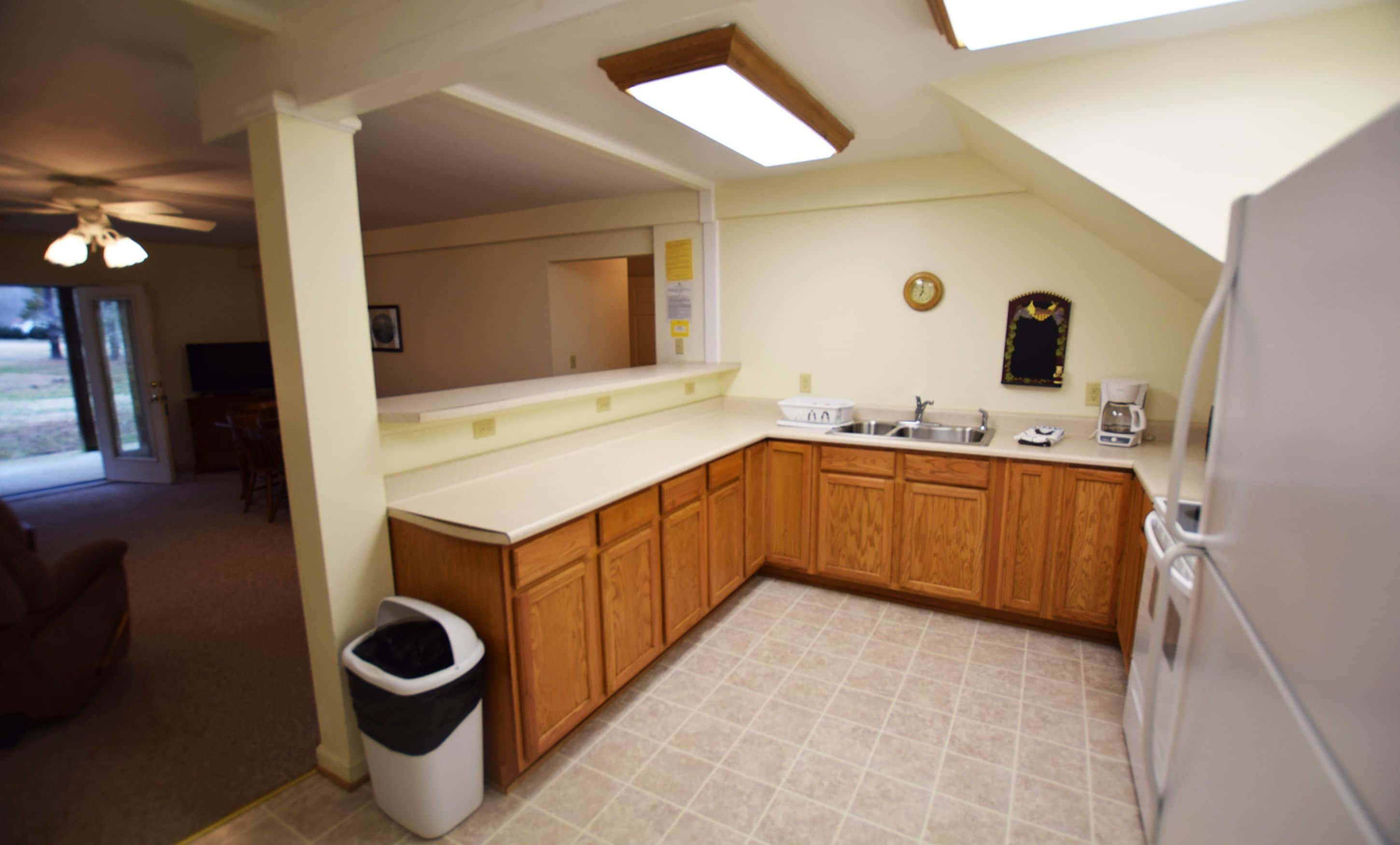 A kitchen with wooden cabinets, a sink, and a trash can.